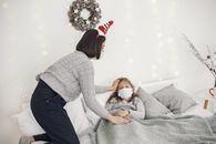 A mother comforts her daughter in bed with festive decor and face masks.