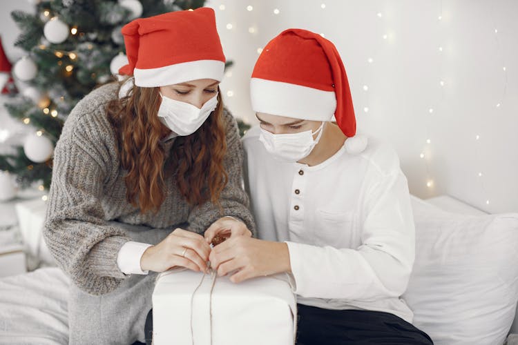 Family In Face Masks And Santa Hats Unwrapping Christmas Gift