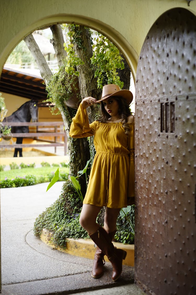 A Woman In Yellow Dress Wearing A Cowboy Hat And Boots Standing On The Doorway