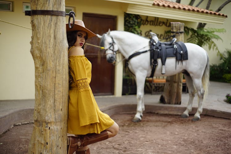 A Woman In Yellow Dress Leaning On A Wooden Post Near A Horse