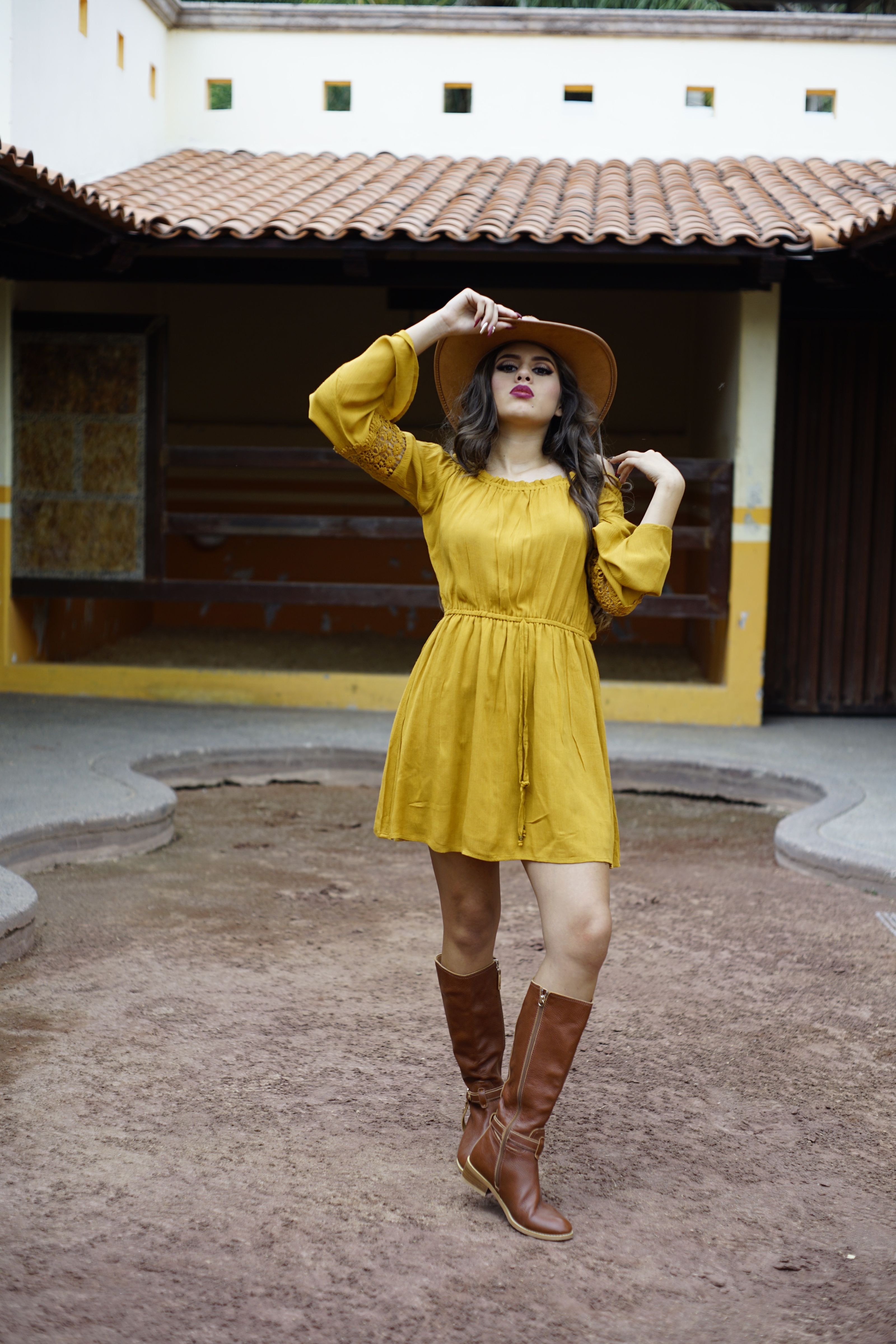 Mulher posando em vestido amarelo com chapéu ao ar livre, mostrando estilo de moda.