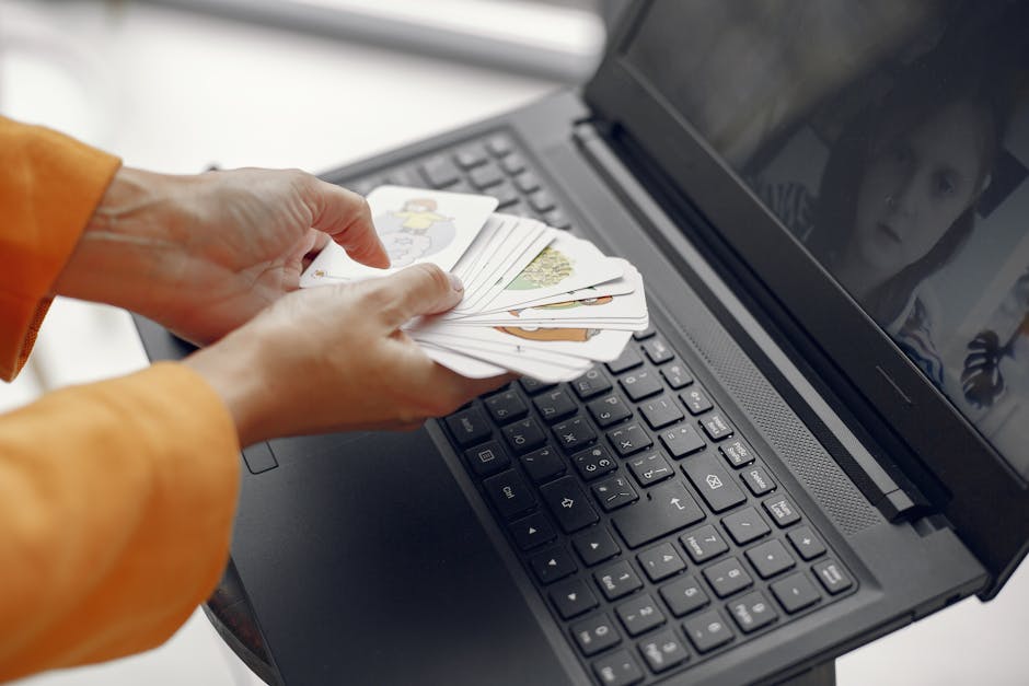 Descript vs CapCut: Auto Captions for Podcasts (2026) Hands holding cards in front of a laptop during an online meeting, with a screen showing a virtual attendee.
