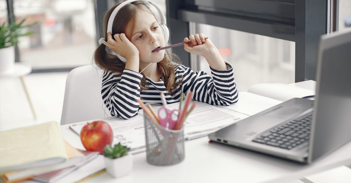 A child wearing headphones doing homework on a laptop indoors. Remote learning setup.