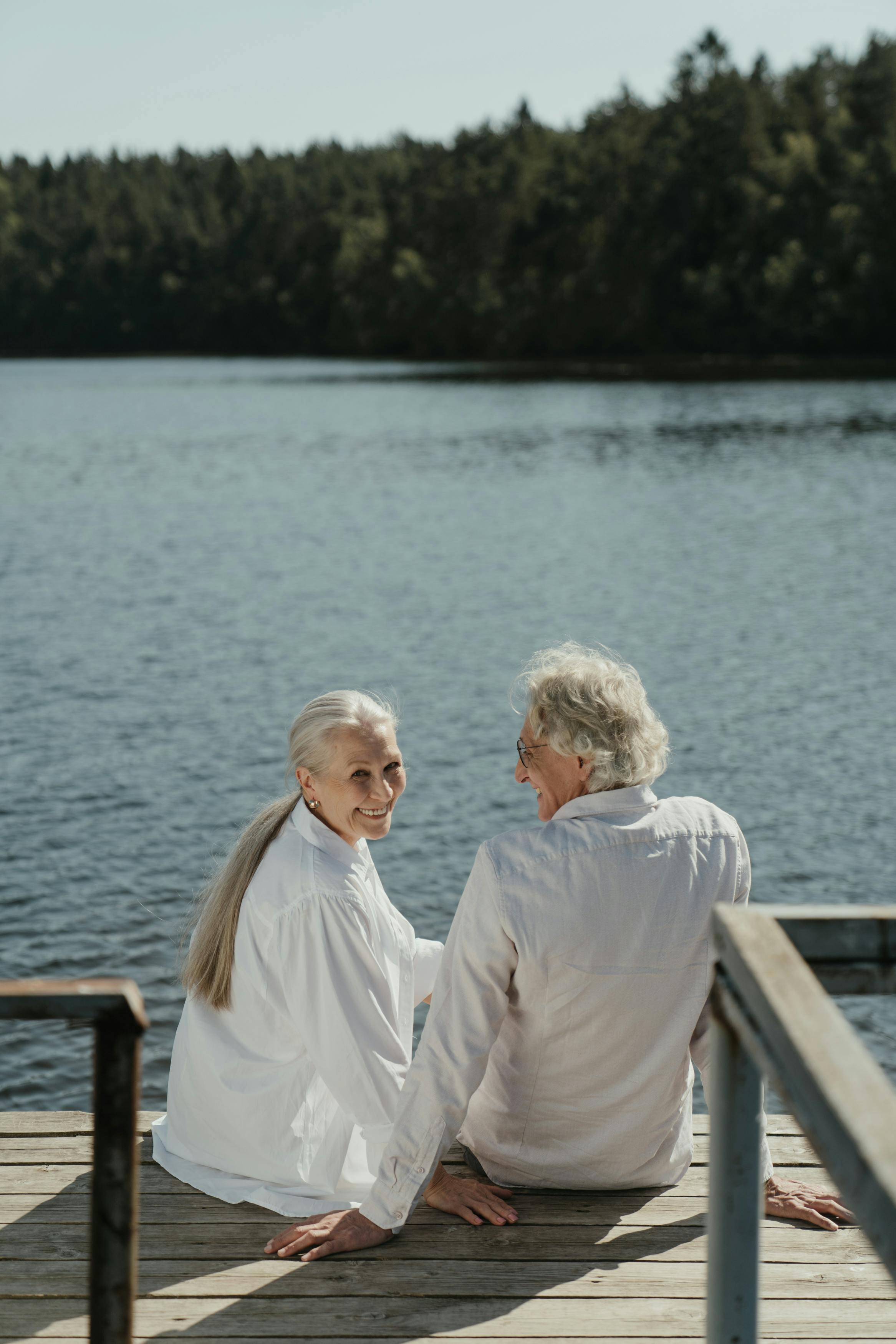 an elderly couple sitting on a wooden dock