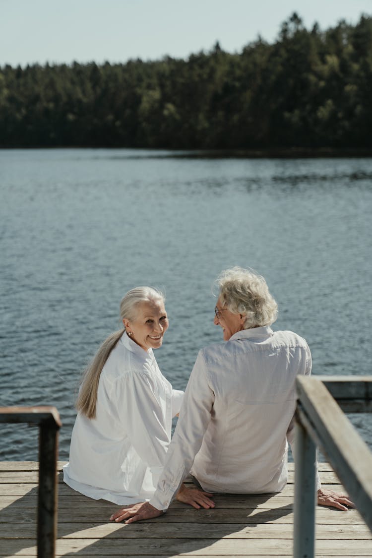 An Elderly Couple Sitting On A Wooden Dock