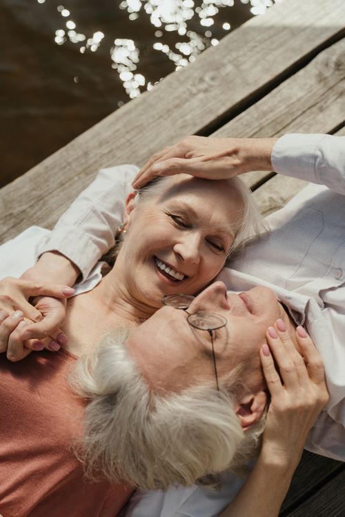Free Elderly couple enjoying a sunny day on a wooden dock by the water, sharing a tender moment. Stock Photo