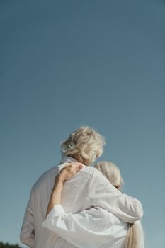 一对老年夫妇在户外宁静的天空下温柔相拥，象征着爱与陪伴