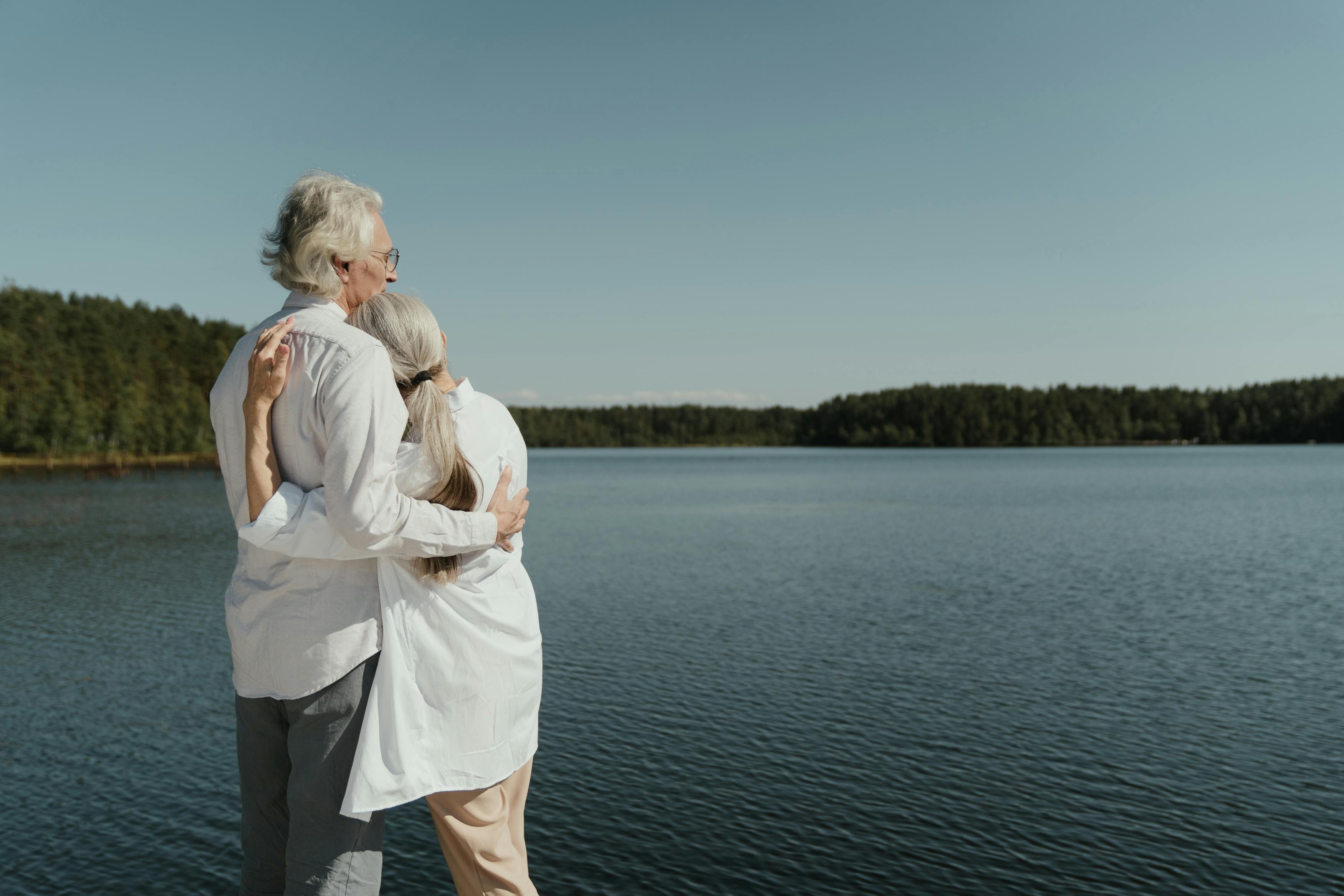 an elderly couple hugging near the lake