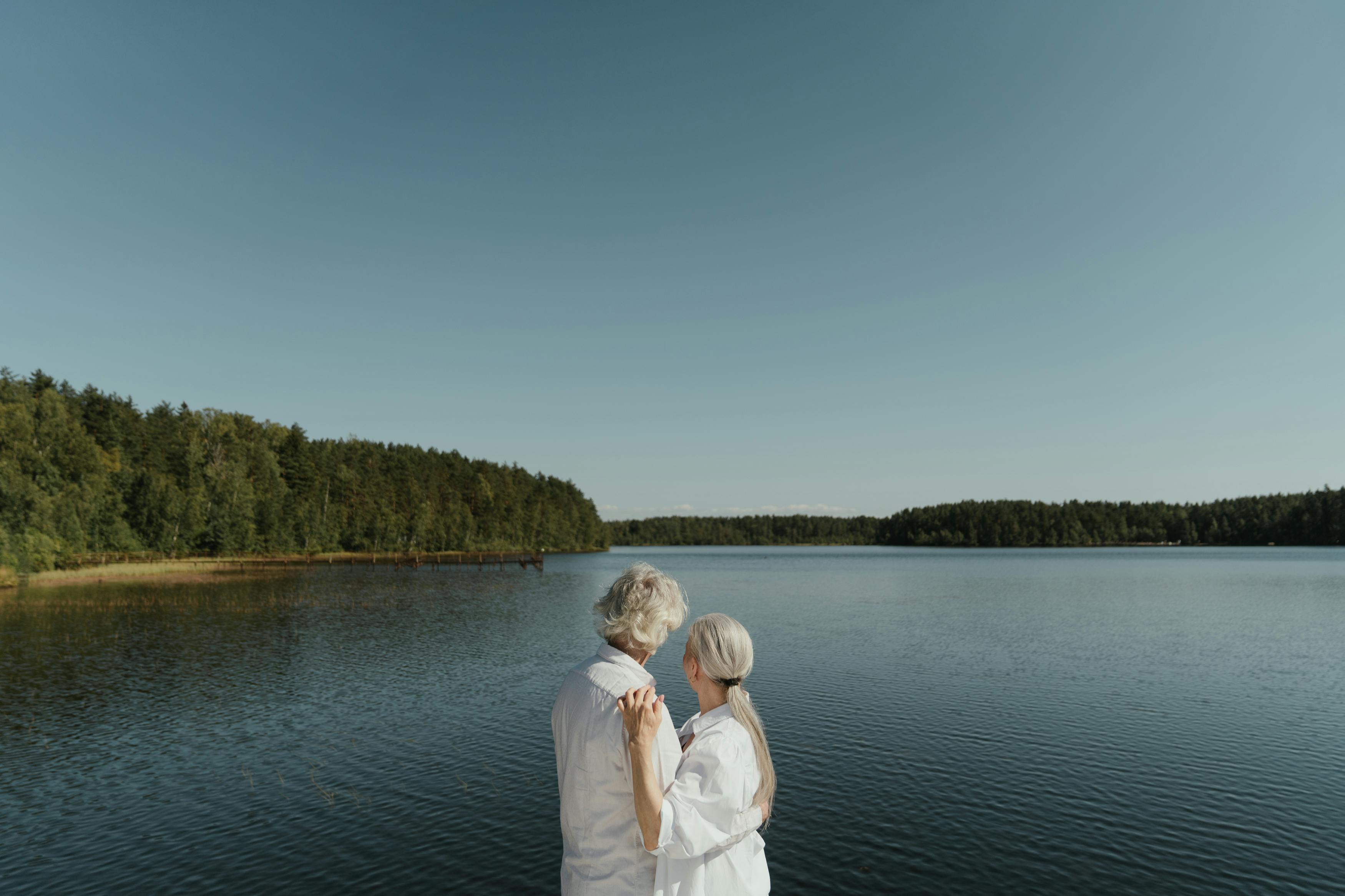 an elderly couple hugging near the lake