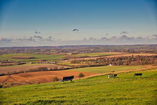 Expansive countryside view with benches, fields, and distant horizon under a clear sky.