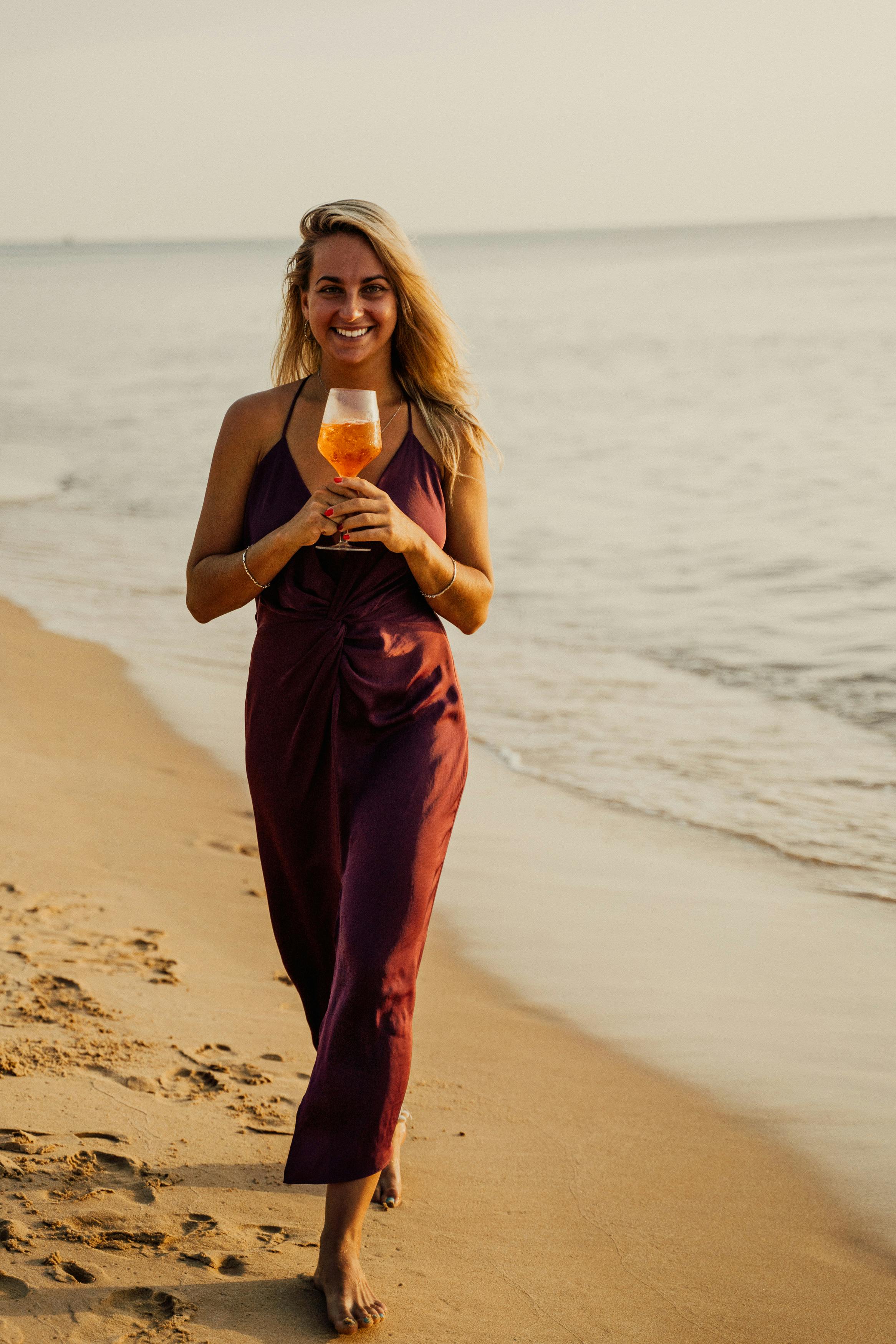 a woman in brown top holding a glass of drink on the beach