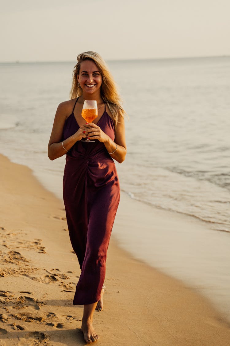 A Woman In Brown Top Holding A Glass Of Drink On The Beach