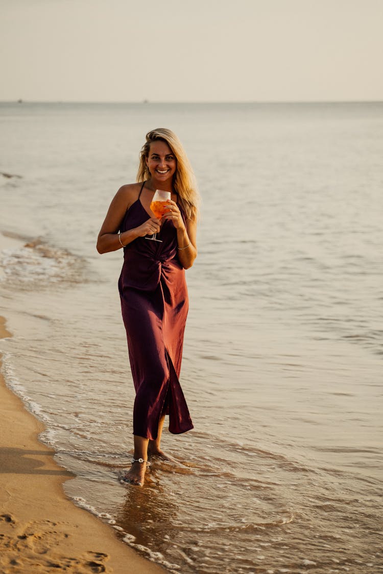 A Woman In Brown Dress Holding A Glass Of Drink On The Beach