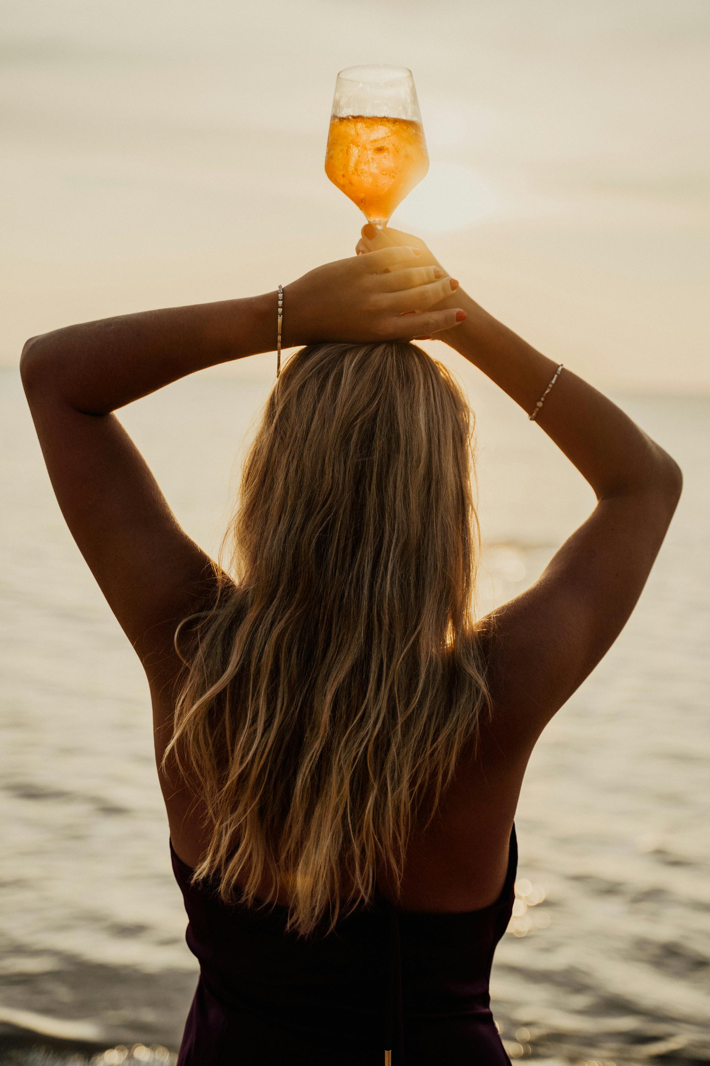 a woman in brown top holding a glass of drink on the beach