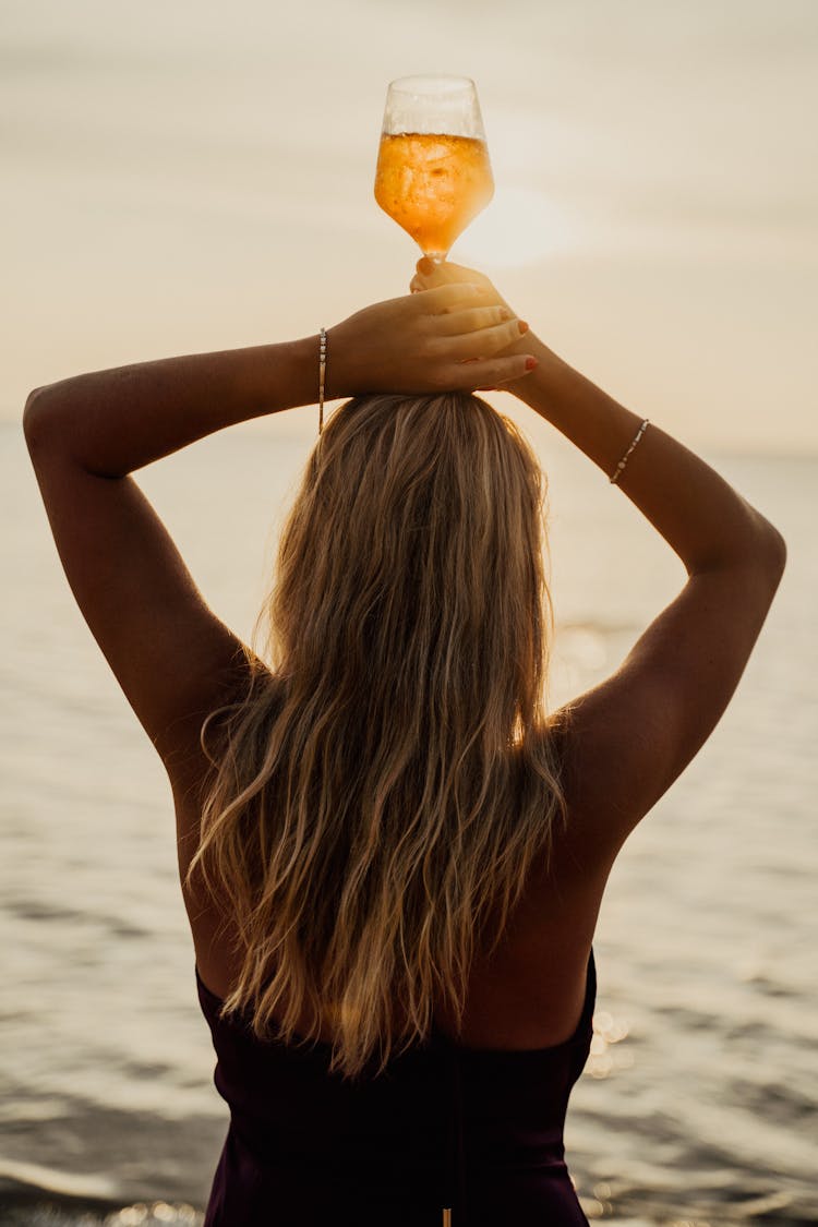 A Woman In Brown Top Holding A Glass Of Drink On The Beach