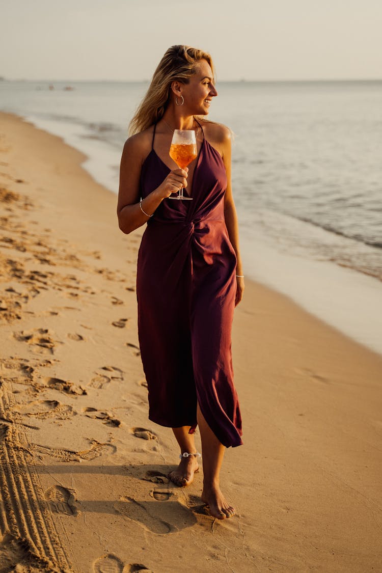 A Woman In Brown Dress Holding A Glass Of Drink On The Beach