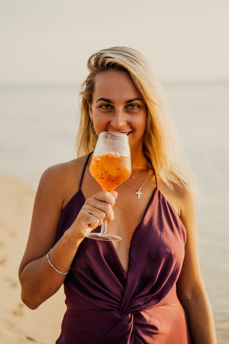 A Woman In Brown Top Holding A Glass Of Drink On The Beach