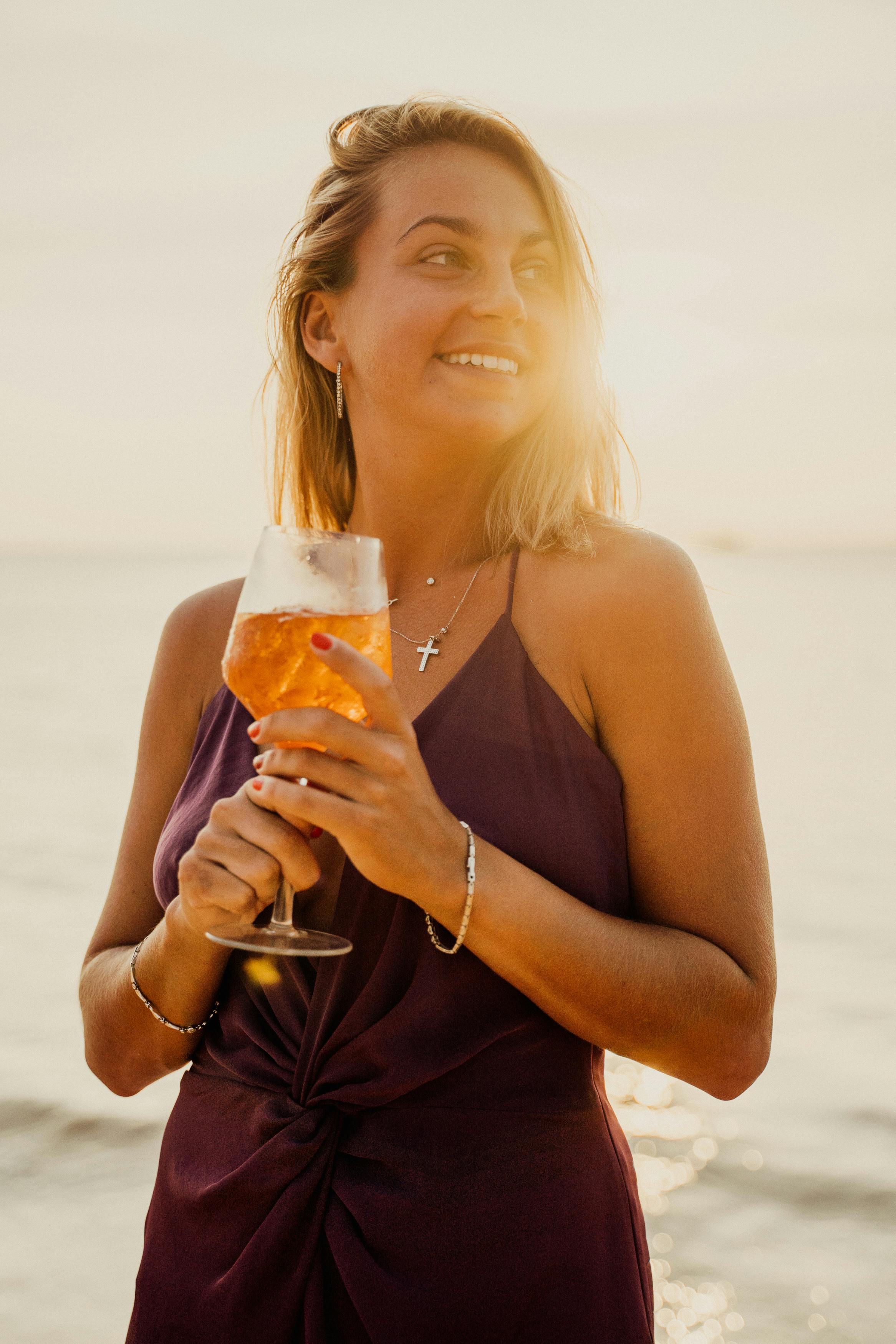 a woman in brown top holding a glass of drink on the beach