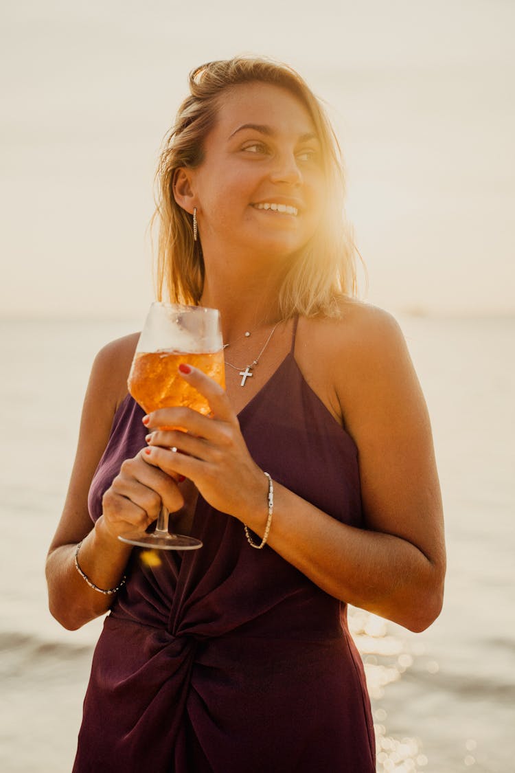 A Woman In Brown Top Holding A Glass Of Drink On The Beach