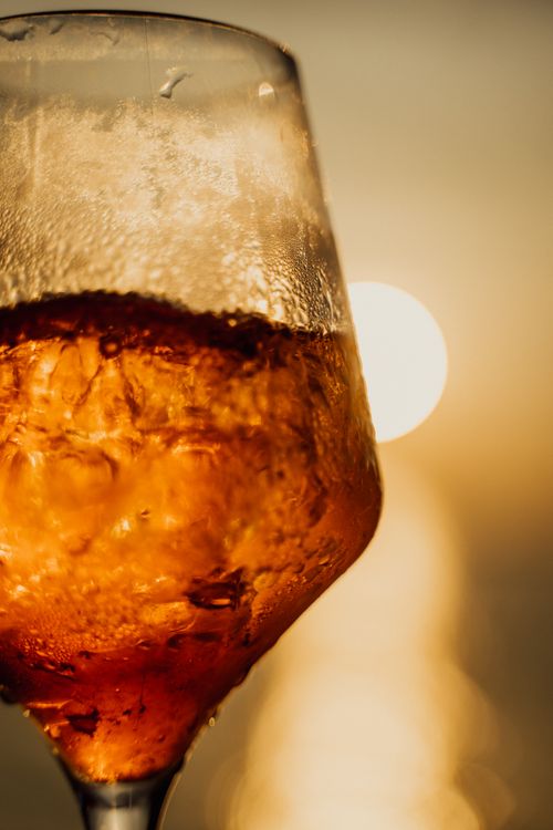 Free Close-up of a chilled wine glass with amber liquid against a sunset backdrop, perfect for summer vibes. Stock Photo