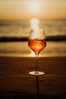 A close-up of a wine glass on the beach during a stunning sunset, evoking relaxation.