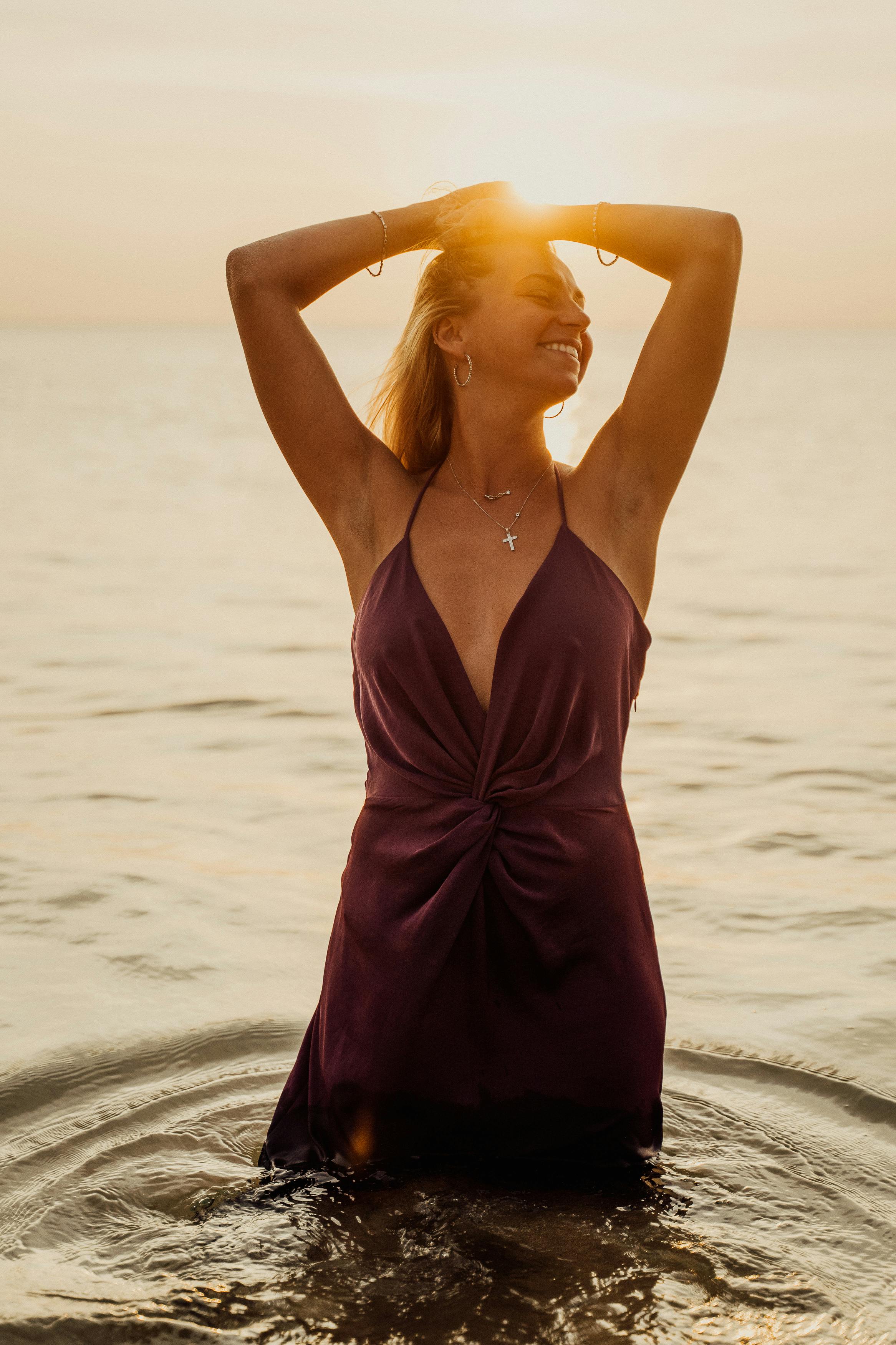 a woman in purple spaghetti strap dress standing on the shore