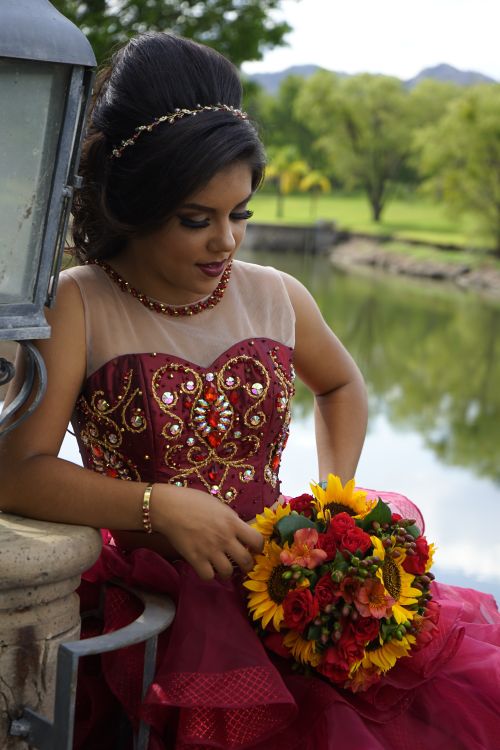 Free Young woman in decorative maroon gown with vibrant bouquet by lakeside setting. Stock Photo