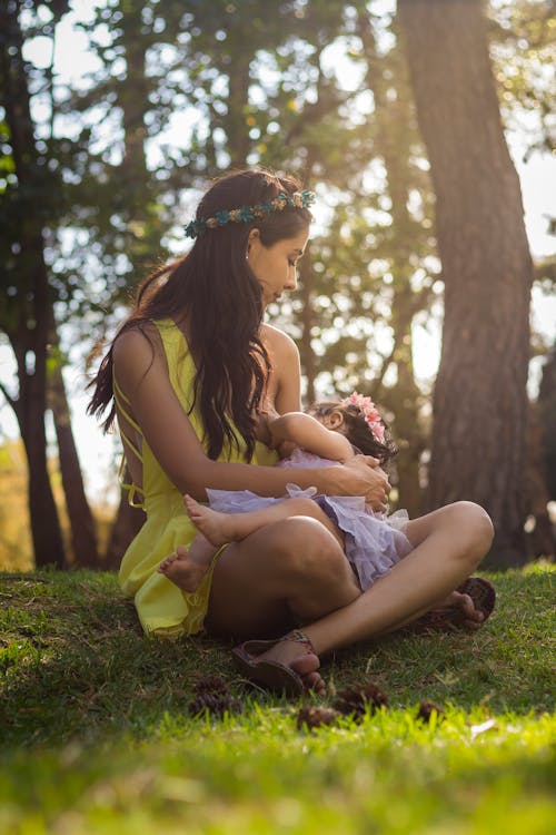 Free Mother Breasfeeding her Child while Sitting on Grass Stock Photo