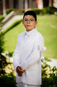 一个穿着白色西装、戴着眼镜的孩子在户外庆祝他的第一次宗教主题圣餐