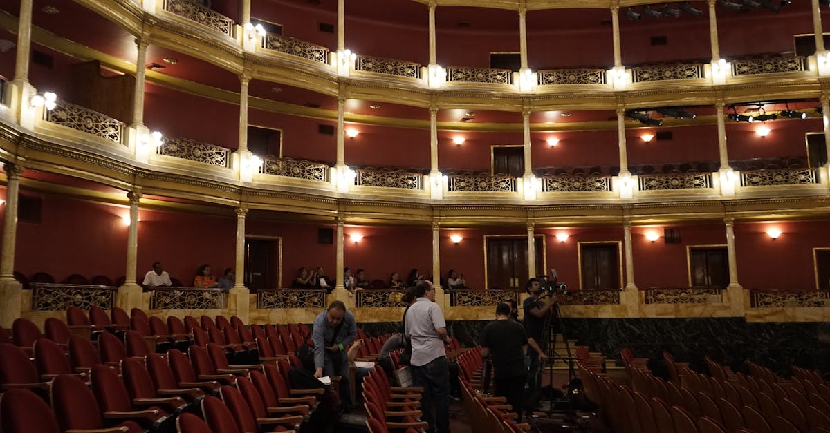 View of a classic theater interior with red seats and a camera crew setting up, capturing the venue's grandeur.