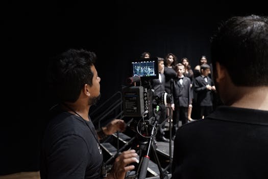 Capture of a cameraman recording a choir of children in formal attire on stage.