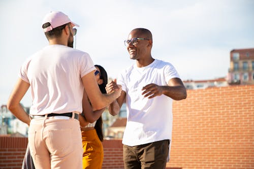 Happy smiling multiethnic male friends greeting each other and shaking hands while gathering on rooftop in urban city