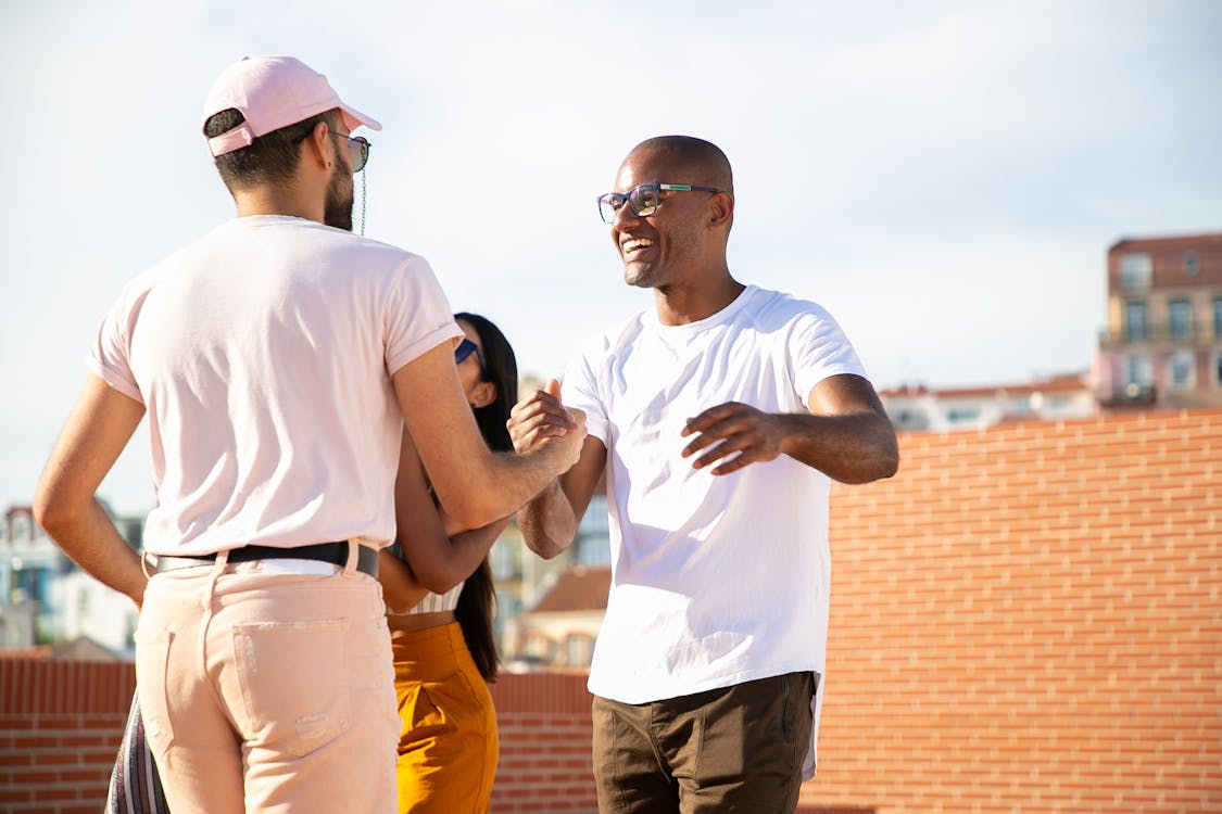 Free Happy smiling multiethnic male friends greeting each other and shaking hands while gathering on rooftop in urban city Stock Photo