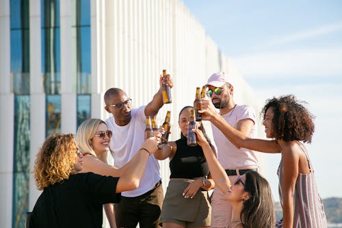 Joyful diverse friends clinking beer bottles on rooftop