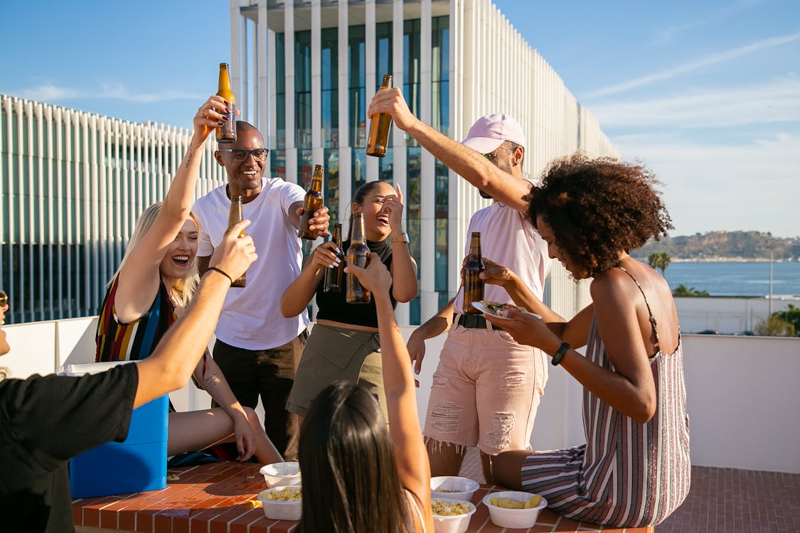 Free Joyful diverse friends toasting with beer bottles on rooftop Stock Photo