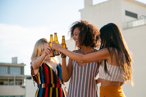 Joyful women clinking beer bottles on rooftop