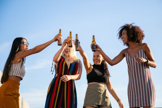 四名女子在户外蓝天下喝着啤酒庆祝，享受休闲聚会