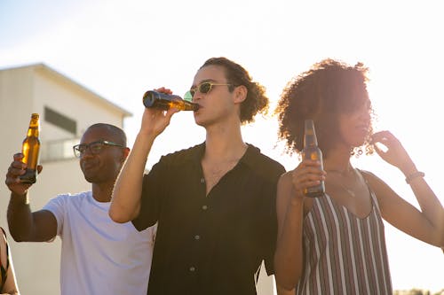 Разнообразные друзья пьют бутылки пива во время вечеринки на открытом воздухе