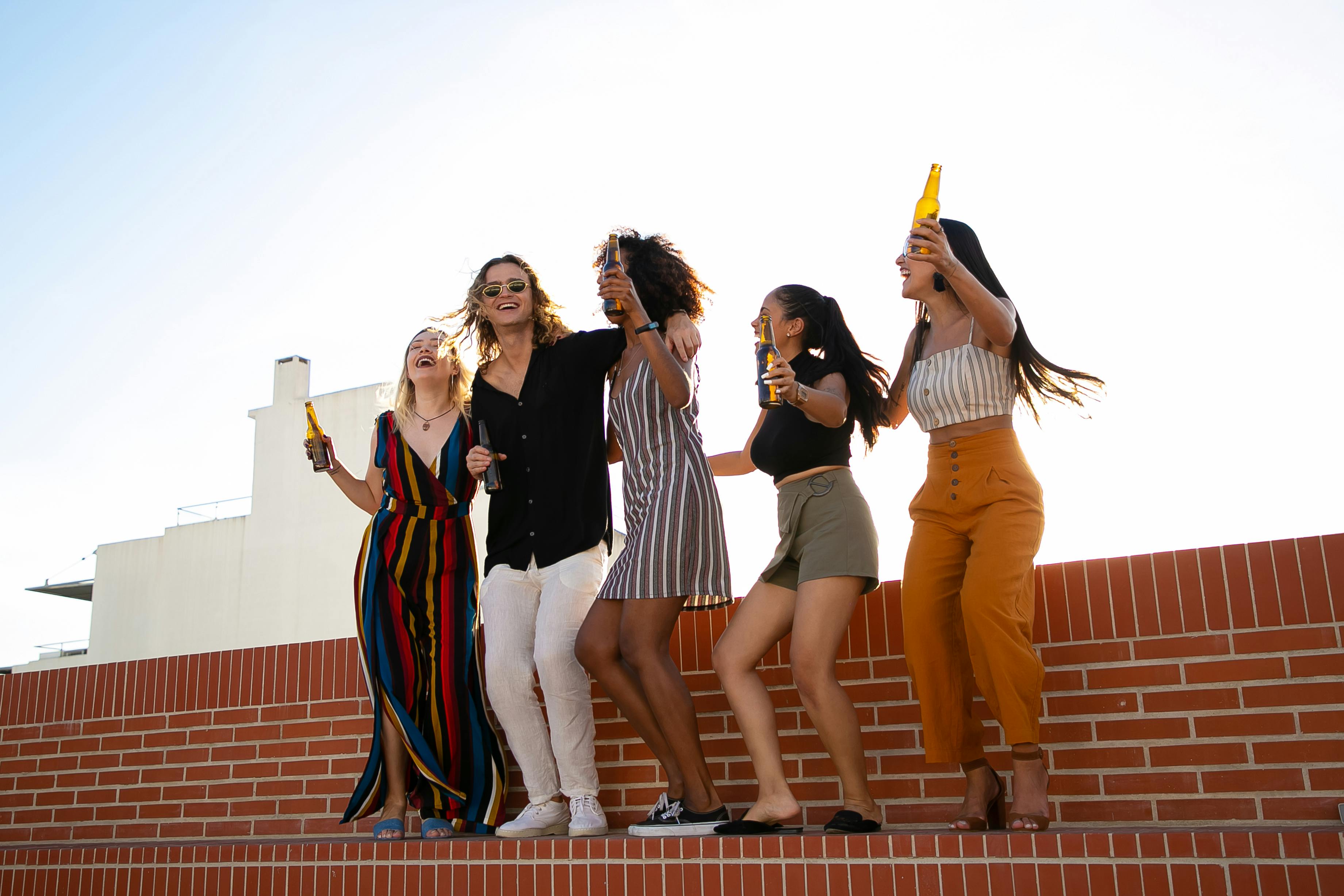 excited multiethnic stylish friends dancing with bottles of beer