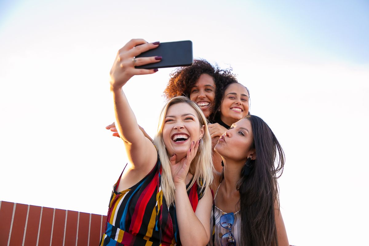 Cheerful friends taking a group selfie on a smartphone outdoors