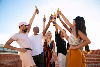 Group of cheerful multiethnic friends clinking beer bottles during event on terrace