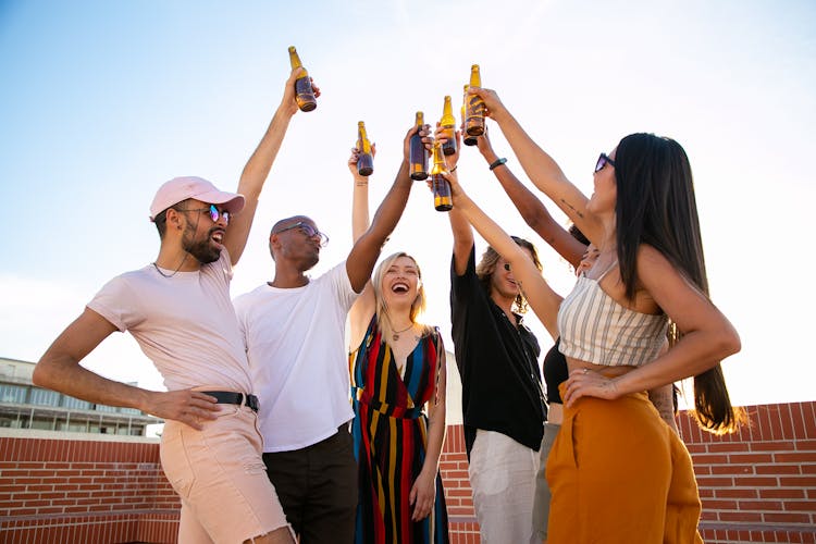 Group Of Cheerful Multiethnic Friends Clinking Beer Bottles During Event On Terrace