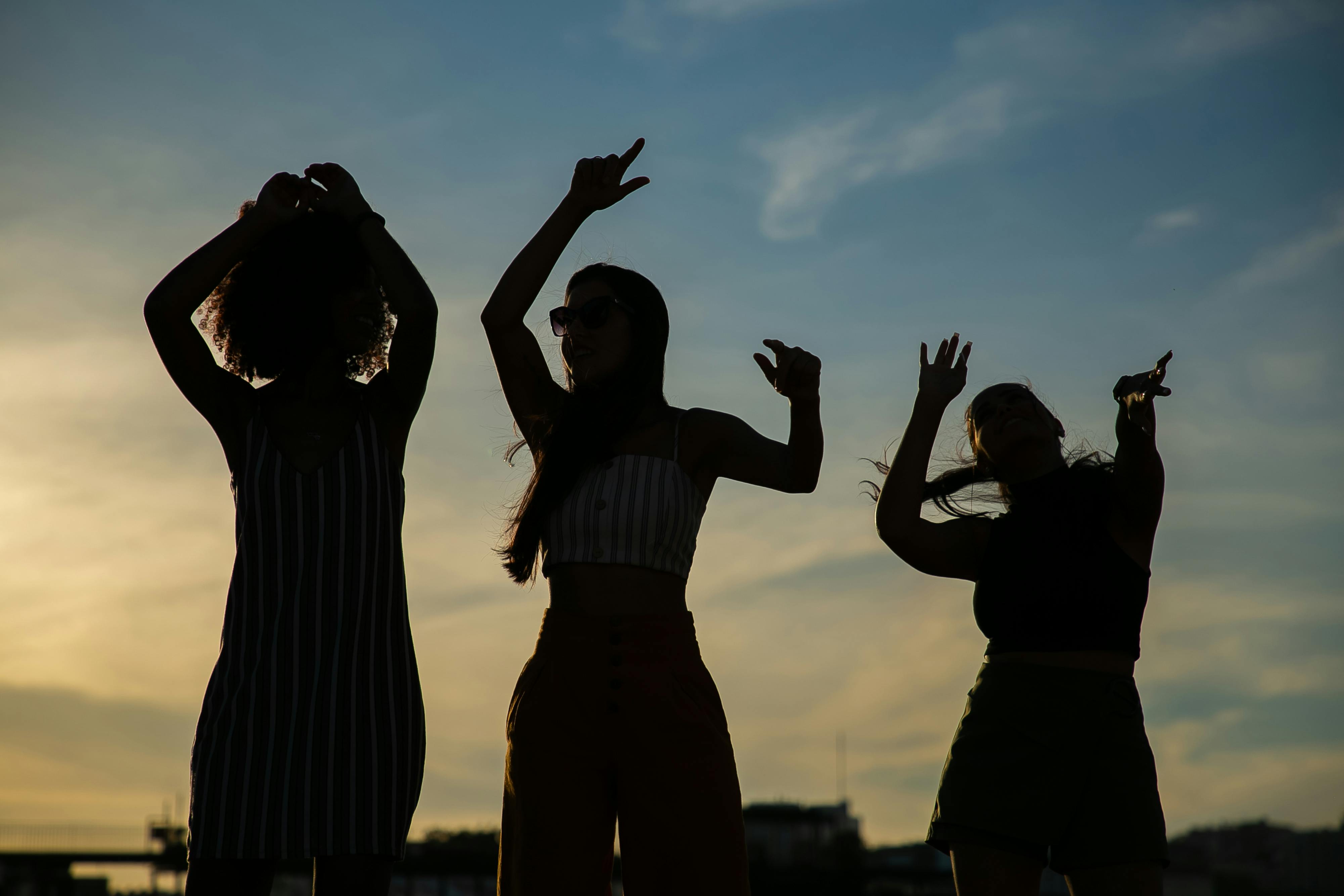 anonymous girlfriends dancing against sunset sky