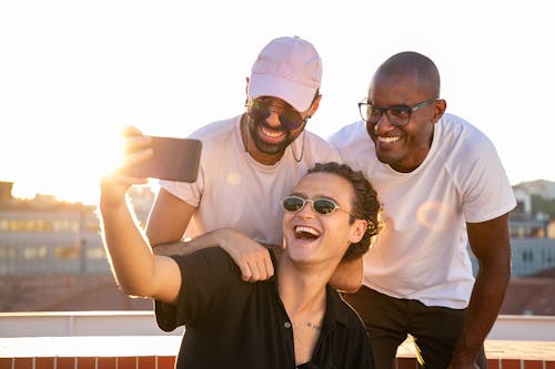 Wesoły, Młodzi Wieloetniczni Mężczyźni, śmiejąc Się I Biorąc Selfie Na Smartfonie W Słońcu