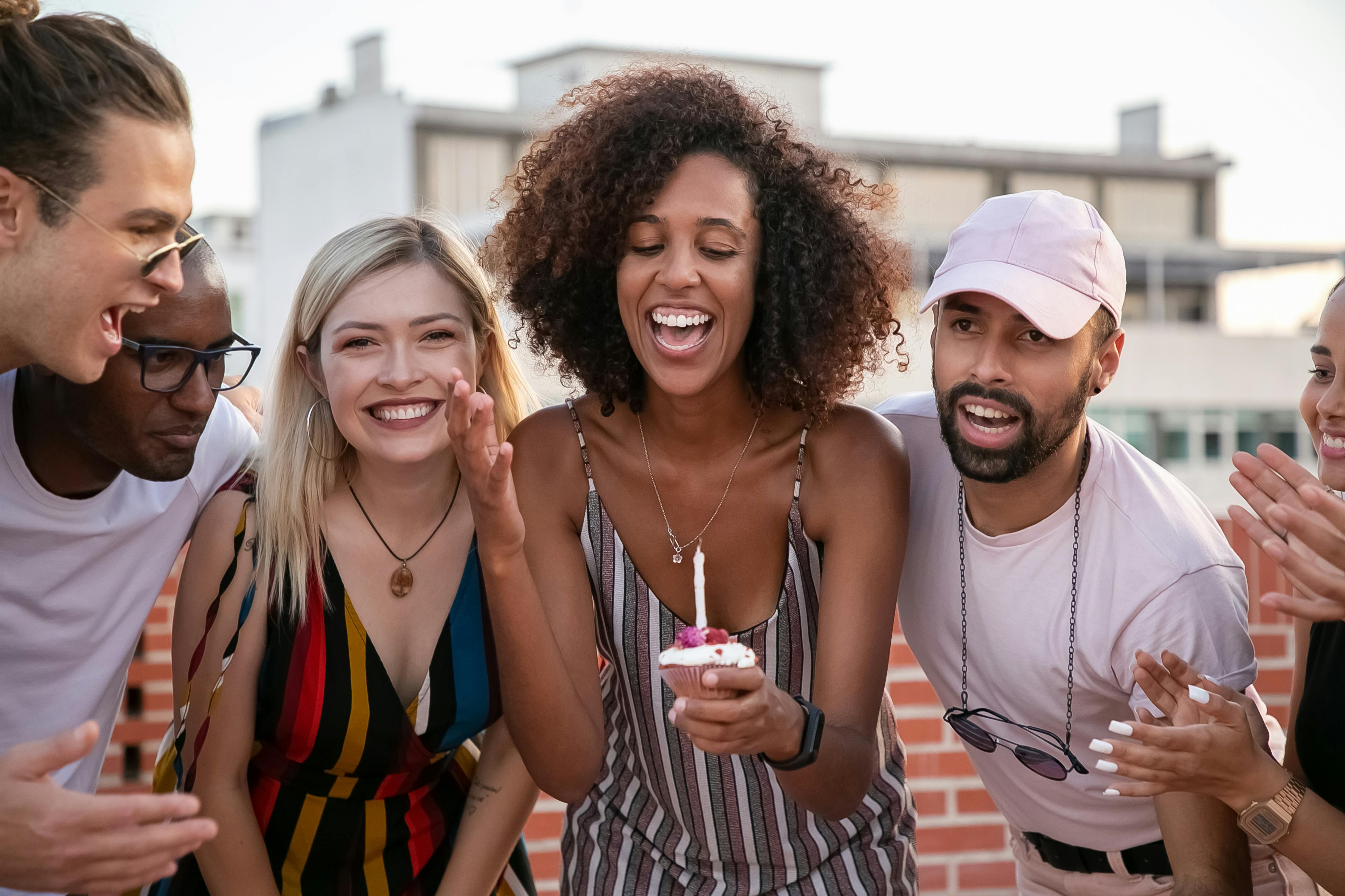 Happy African American woman blowing out candle during birthday party with diverse friends