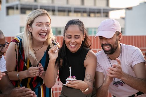 Free Cheerful young diverse friends laughing and clapping hands while young ethnic lady making wish and blowing out candle on cupcake during open air birthday party Stock Photo