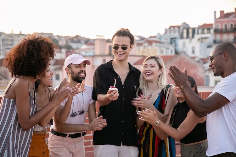 Joyful Young Man With Birthday Cupcake In Hand During Party With Happy Diverse Friends