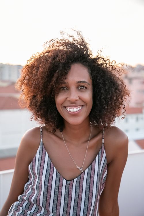 Free Cheerful woman with curly hair smiling joyfully at sunset on a balcony in Portugal. Stock Photo