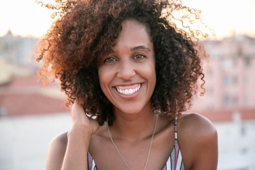 Free Happy woman with curly hair and brown eyes smiling outdoors. Stock Photo
