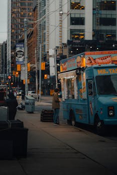 A person buying food at a vibrant truck in downtown Toronto during twilight.